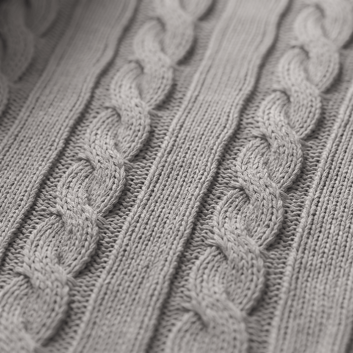 Grey cable knit sweater fabric close-up with textured braided pattern.